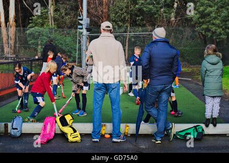 Les parents et l'entraîneur de regarder les jeunes joueurs de hockey sur le terrain avant un match chaud en hiver, Melbourne, Australie. Banque D'Images