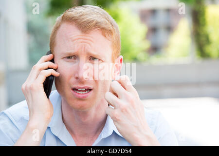 Closeup portrait, inquiets à l'jeune homme en chemise bleue parlant au téléphone à quelqu'un, à la sombre, isolé à l'extérieur extérieur background Banque D'Images