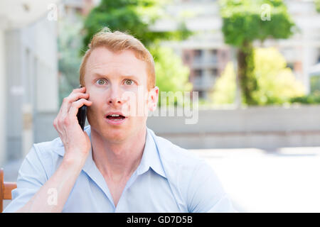 Closeup portrait jeune homme, choqué, surpris, bouche grande ouverte, par ce qu'il entend sur le téléphone cellulaire, Bâtiment isolé à l'extérieur Banque D'Images