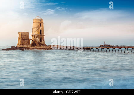 Vieux phare ruiné par mer au coucher du soleil Banque D'Images