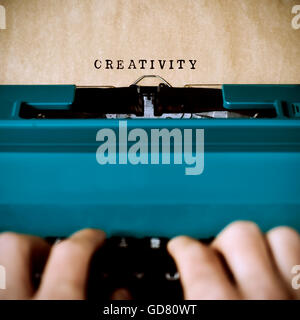 Gros plan des mains d'un jeune homme à écrire le mot créativité dans une feuille jaunâtre avec une vieille machine à écrire bleu Banque D'Images