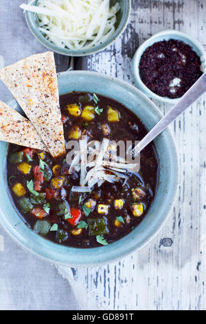 Soupe de haricots noirs surmontés de poivrons rôtis, cilanrto, fromage et ancho croustilles sur un fond de bois/blanc rustique shot Banque D'Images