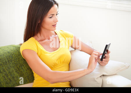 Femme calme en chemise jaune en utilisant un smartphone alors qu'il était assis à l'intérieur Banque D'Images