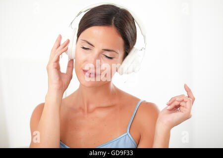 Femme intelligente avec les yeux fermés en blouse bleue se détendre en écoutant de la musique à sa maison Banque D'Images