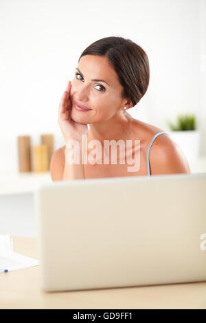 Femme en blouse bleue sophistiquée travaillant sur son ordinateur portable dans sa maison Banque D'Images