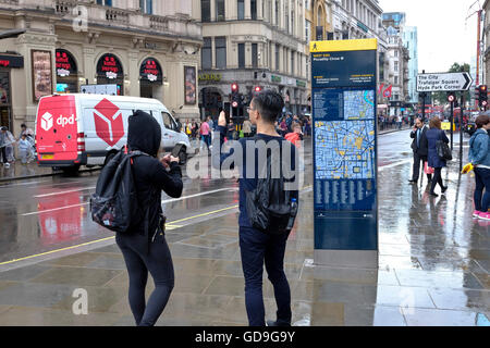 Piccadilly Circus Londres. Un touriste chinois prend une photo d'Eros avec son téléphone intelligent à l'état humide et pluvieux jour dans Piccadilly Circus Londres Banque D'Images