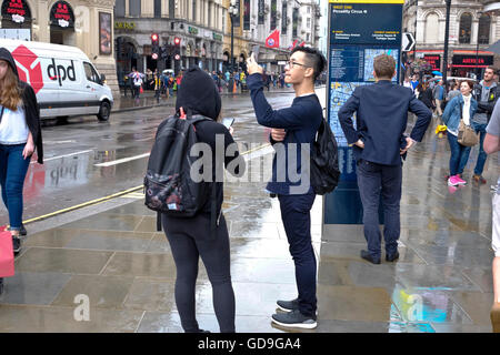 Piccadilly Circus Londres. Un touriste chinois prend une photo d'Eros avec son téléphone intelligent à l'état humide et pluvieux jour dans Piccadilly Circus Londres Banque D'Images