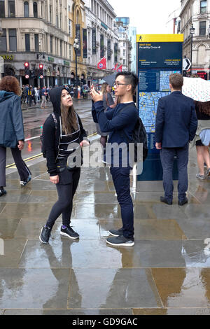 Piccadilly Circus Londres. Un touriste chinois prend une photo d'Eros avec son téléphone intelligent à l'état humide et pluvieux jour dans Piccadilly Circus Londres Banque D'Images