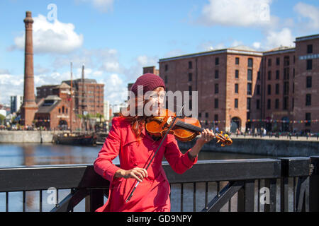 Une femme de rue jouant le violon ou le violon avec Albert Dock en arrière-plan, dans le pays des quais de Liverpool. Bus sur la promenade côtière au bord de la rivière, sur le front de mer de Liverpool, à Merseyside, au Royaume-Uni. Le Pier Head est une attraction touristique centrale avec plusieurs monuments remarquables et des développements modernes qui concentrent l'attention sur la longue histoire et le patrimoine des villes en tant que port principal sur le Mersey. Banque D'Images