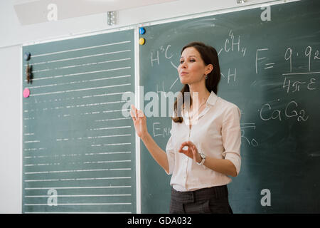 Jeune femme heureuse de parler à l'enseignant permanent classe contre green board Banque D'Images