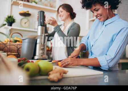 Jeune femme africaine fruits coupe au comptoir du bar, avec un collègue à l'aide de centrifugeuse en arrière-plan. Deux femmes travaillant au bar à jus. Banque D'Images