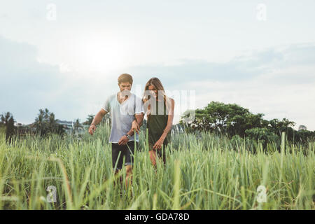 Piscine shot of young couple walking through grass field. L'homme et la femme marche dans la nature. Banque D'Images