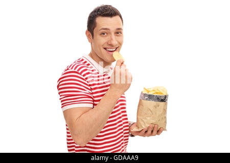 Young cheerful guy eating potato chips et regardant la caméra isolé sur fond blanc Banque D'Images