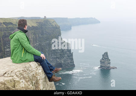 L'Irlande, le comté de Clare, les Falaises de Moher, homme assis en hauteur sur un rocher Banque D'Images