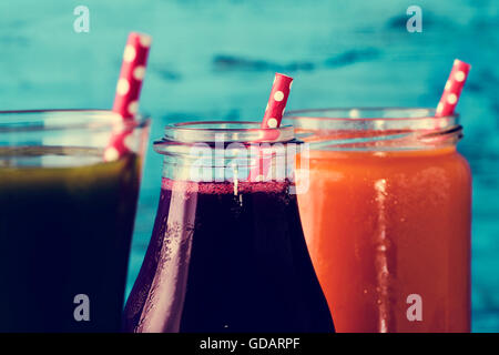 Libre de trois différents smoothies frais servi dans un verre, un bocal en verre et une bouteille de verre rouge à motifs avec des pailles Banque D'Images