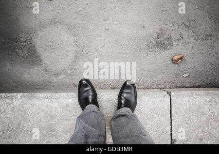 Pieds d'un homme en noir citadin nouveau cirer les chaussures debout sur trottoir gris Banque D'Images