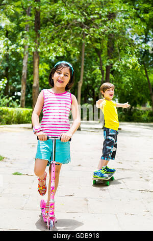 Les enfants indiens 2 garçon et fille amis pousser Scooter et patinage à roulettes Banque D'Images