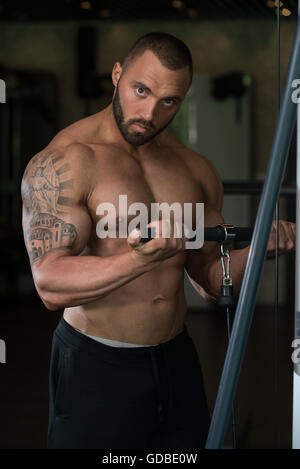 Big Tattooed Man dans le sport est l'exercice de biceps sur la Machine - Modèle musculaire Bodybuilder athlétique dans l'exercice au centre de remise en forme Banque D'Images