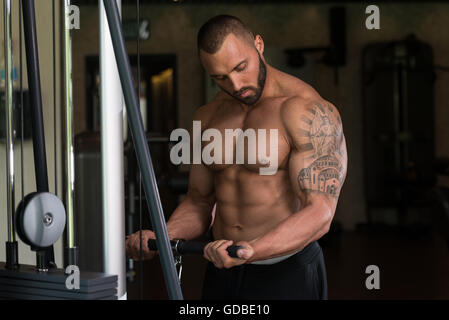 Big Tattooed Man dans le sport est l'exercice de biceps sur la Machine - Modèle musculaire Bodybuilder athlétique dans l'exercice au centre de remise en forme Banque D'Images