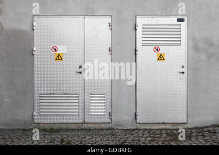 Les portes métalliques avec des panneaux d'avertissement de tension élevée dans l'industrie de béton gris, texture mur de fond photo, vue de face Banque D'Images