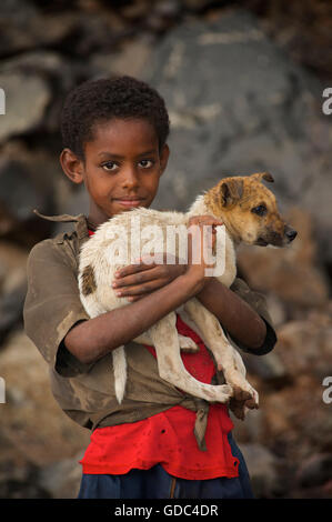 Boy holding éthiopien chien timide. La route d'écorcer, Éthiopie. Banque D'Images