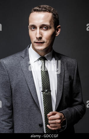 L'homme d'affaires graves de visage expressif portant costume et cravate gris. Isolé sur fond sombre. Banque D'Images