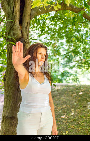 S'arrêter et parler à mon geste de la main par busty femme mature chic avec des sentiments négatifs contre green garden background with copy space Banque D'Images