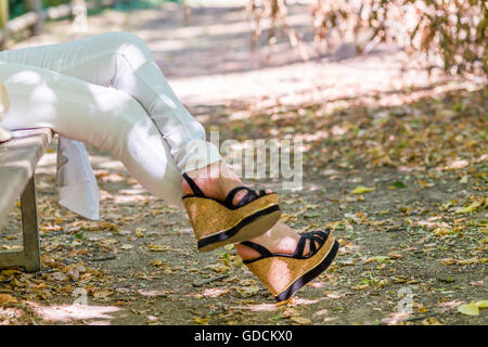 Jambes de femme assis sur un banc dans un pantalon blanc et des chaussures plate-forme Banque D'Images