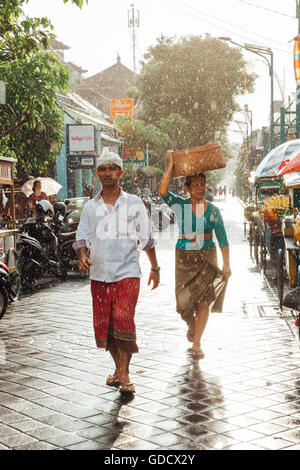 L'homme et de la femme indonésienne en vêtements traditionnels de marcher sous la pluie sur la rue de Kuta, Indonésie Banque D'Images