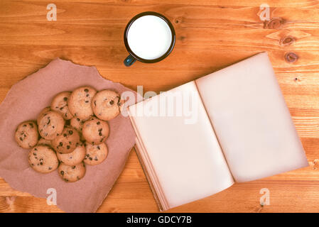 Des cookies aux pépites de chocolat, lait tasse et ouvert livre vintage sur table en bois rustique, vue du dessus Banque D'Images