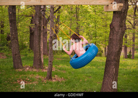 Boy swinging sur balançoire pneu en forêt Banque D'Images