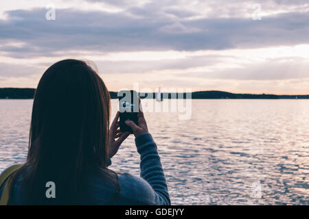 Femme de prendre une photo de bateau naviguant sur l'océan au coucher du soleil Banque D'Images