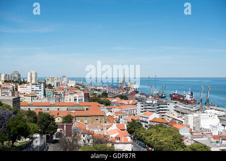 Paysage urbain du port de Lisbonne Pont Vasco de Gama Portugal | LISBONNE, Portugal — Une vue en hauteur sur les toits de Lisbonne permet de voir le port de travail de Lisbonne et, à l'horizon, le pont Vasco de Gama traversant l'estuaire du Tage. Achevé en 1998 pour marquer le 500e anniversaire du voyage de Vasco de Gama vers l'Inde, le pont s'étend sur environ 7,6 miles (12,3 km) et est le plus long du Portugal. Des grues et des navires conteneurs bordent le front de mer sous le quartier résidentiel aux toits de terre cuite au premier plan. Banque D'Images
