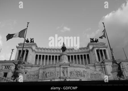 Altare della Patria, hommage monumental de Rome à l’unité et à la nation, capturé en noir et blanc saisissant avec des drapeaux hissés sous un ciel spectaculaire. Banque D'Images