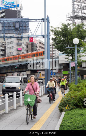 Deux cyclistes vélo parmi les locaux dans le centre d'Osaka. Banque D'Images