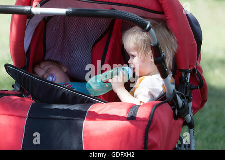 Enfants, jumeaux dans une poussette, été chaud, un tout-petit buvant dans une tasse à bec Banque D'Images