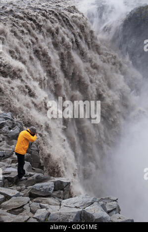 Islande : un homme avec un imperméable jaune prendre des photos de Dettifoss, l'une des plus puissantes en cascade l'Europe, célèbre pour ses paysages exotiques Banque D'Images