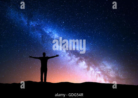 Paysage de nuit avec Voie Lactée. Silhouette d'un jeune homme debout avec les bras levés sur la montagne. Bel Univers. Trav Banque D'Images
