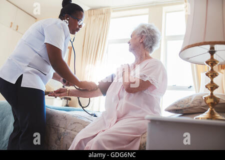 Contrôle de la pression artérielle une infirmière d'un senior woman sitting on bed at home. Accueil Contrôle de la pression artérielle soignant les patients à l'ho Banque D'Images