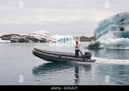 Islande : l'homme sur un canot entre la glace, les icebergs dans la lagune glaciaire du Jökulsárlón, un lac glaciaire dans le Parc National de Vatnajökull Banque D'Images