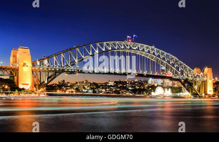 Vue latérale du Sydney Harbour Bridge référence architecturale au coucher du soleil. Passage du pont illuminé se reflétant dans les eaux trouble Banque D'Images