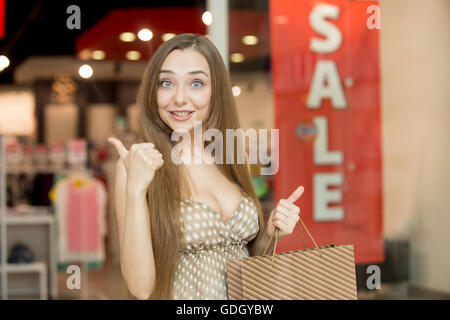 Portrait of attractive young woman in excité shopping centre holding Thumbs up surpris et heureux portant un shopping Banque D'Images