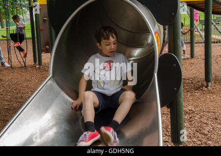 Un jeune garçon apparaît au bas de la diapositive dans une aire de jeux pour enfants dans la région de Prospect Park, lecture. Banque D'Images