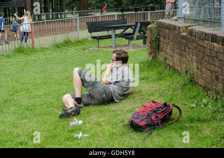 Un homme se détend sur un patch d'herbe dans le parc tout en prenant un appel téléphonique sur son téléphone mobile. Banque D'Images