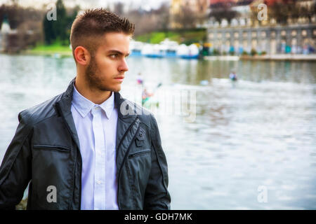 Trois-quarts de la lumière contemplative brown haired young man wearing jeans et blouson gris debout à côté picturesq Banque D'Images