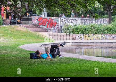 Loisirs et détente, l'homme étendu sur l'herbe et lecture réserve en parc public à côté d'un étang Banque D'Images