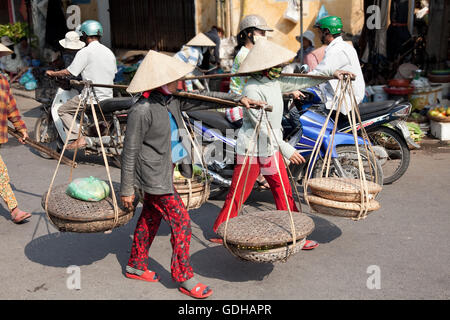 Les femmes avec les chapeaux coniques transportant des légumes sur l'épaule. Banque D'Images