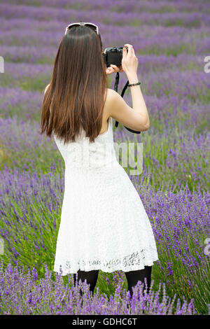 Les visiteurs apprécient la lavande lors d'une journée portes ouvertes à la ferme de Lordington Lavender, Lordington, Chichester, West Sussex Royaume-Uni en juillet - jeune femme prenant une photo Banque D'Images