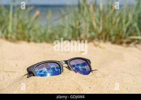 Lunettes de soleil sur plage de sable en raison. Mer et l'herbe sur arrière-plan flou Banque D'Images