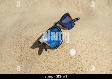 Lunettes de soleil sur plage de sable fin qui reflète avec shell. Selective focus Banque D'Images